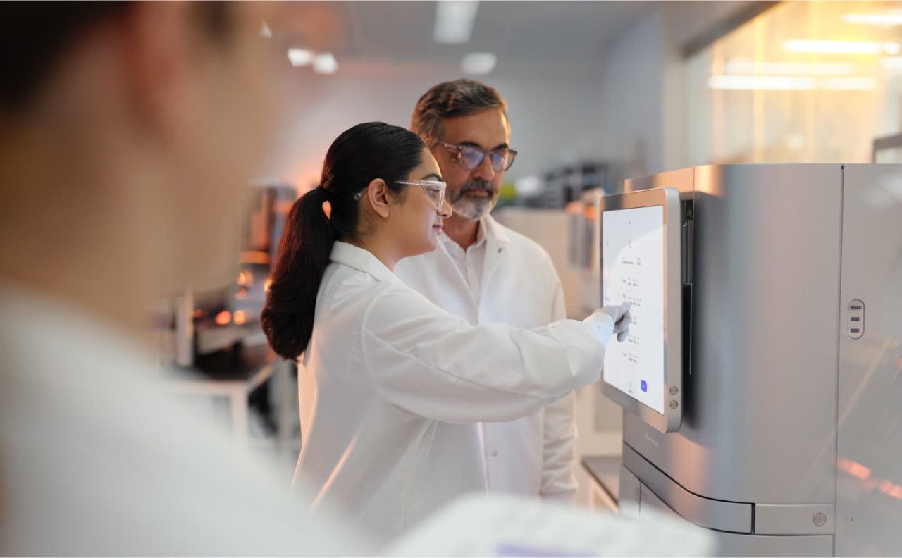 Profile image of male and female scientists reviewing the run setup screen, in the foreground a female scientist is holding a 1.5 reagent in her hands. 