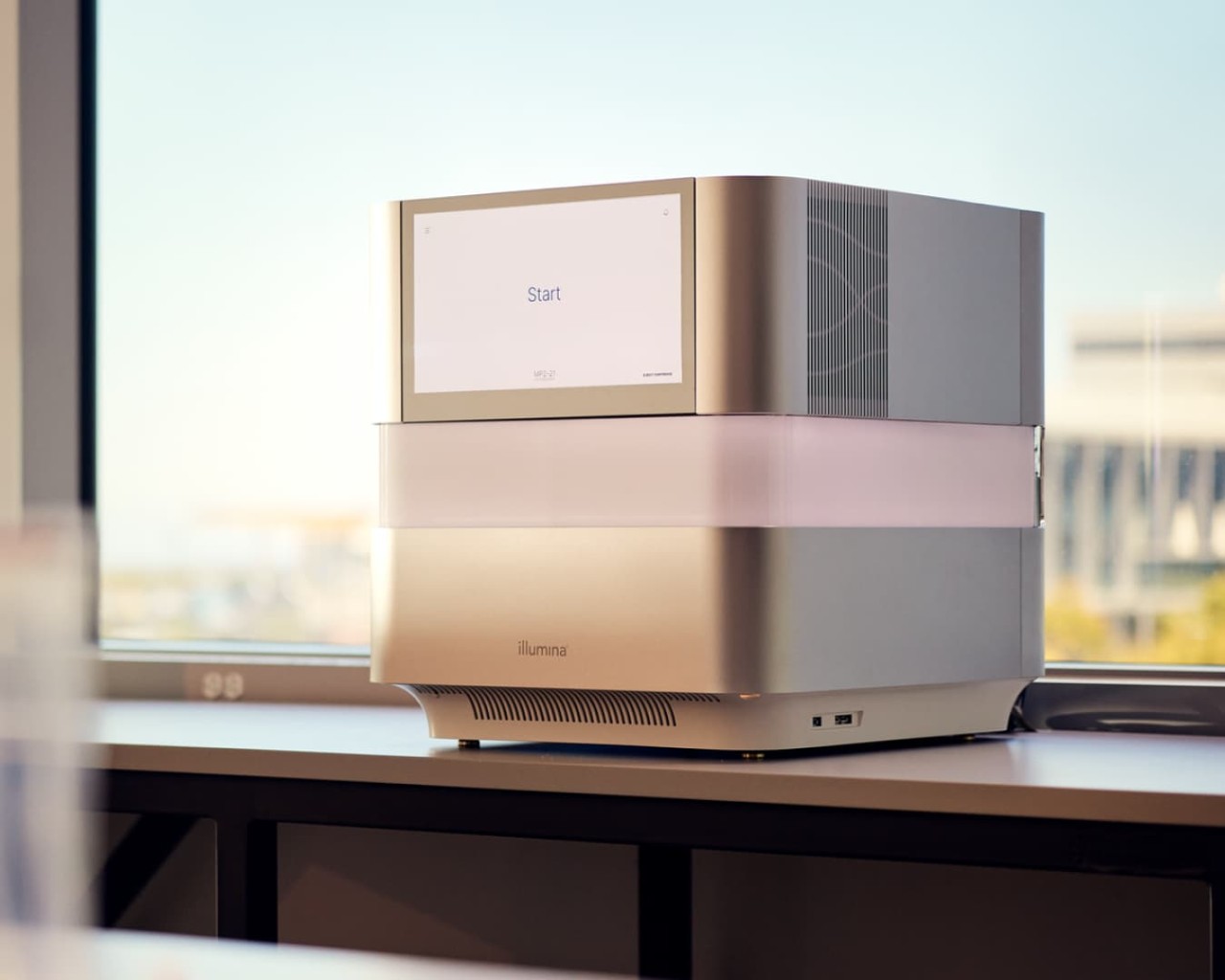 NextSeq 1000/2000 in dry lab in front of a window displaying start screen, blurry foreground